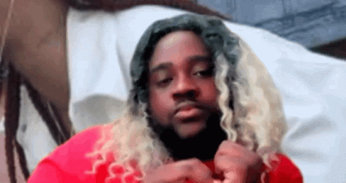 A Man With Long Blonde Hair And Dreadlocks Is Wearing A Red Shirt And Looking At The Camera . GIF