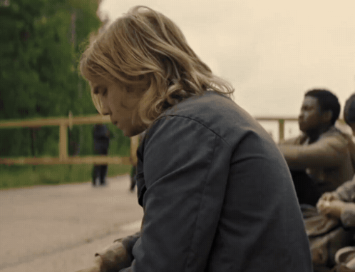 A Man With Long Blonde Hair Is Sitting On A Bench GIF