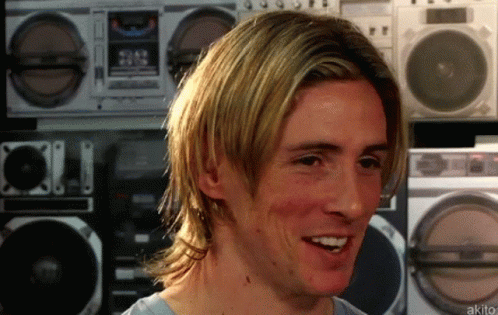 A Man With Long Blonde Hair Is Smiling In Front Of A Row Of Boomboxes GIF