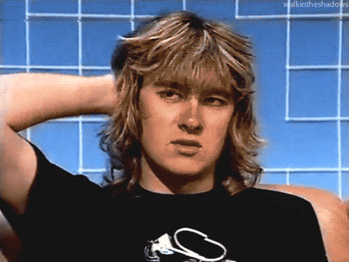 a man with long blonde hair is wearing a black t-shirt with a s on it