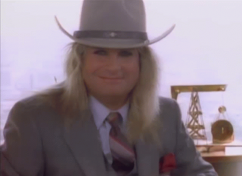 A Man With Long Blonde Hair Wearing A Cowboy Hat And Suit GIF