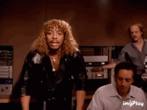 A Man With Long Curly Hair And A Mustache Is Dancing In A Room . GIF