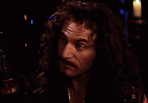 A Man With Long Curly Hair And A Mustache Looks At Something In The Dark GIF