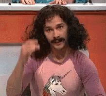 A Man With Long Curly Hair And A Mustache Wears A Pink Shirt With A Unicorn On It GIF