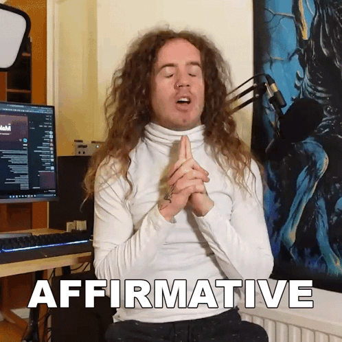 A Man With Long Curly Hair Is Sitting In Front Of A Computer And Says Affirmative GIF