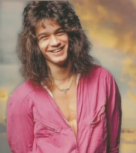 A Man With Long Curly Hair Is Smiling And Wearing A Pink Shirt GIF