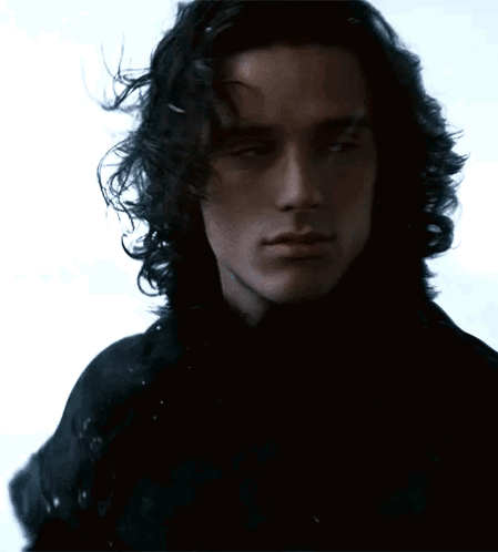 A Man With Long Curly Hair Is Wearing A Black Shirt GIF