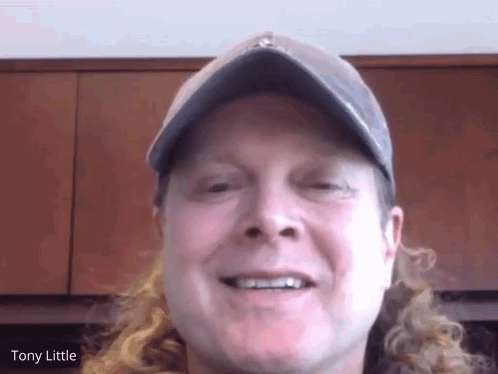 A Man With Long Curly Hair Wearing A Hat And Smiling With The Name Tony Little On The Bottom GIF