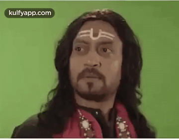 A Man With Long Hair , A Beard And A Tattoo On His Forehead Is Wearing A Red Jacket . GIF