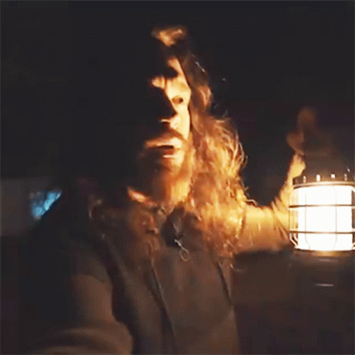 A Man With Long Hair And A Beard Is Holding A Lantern In His Hand GIF
