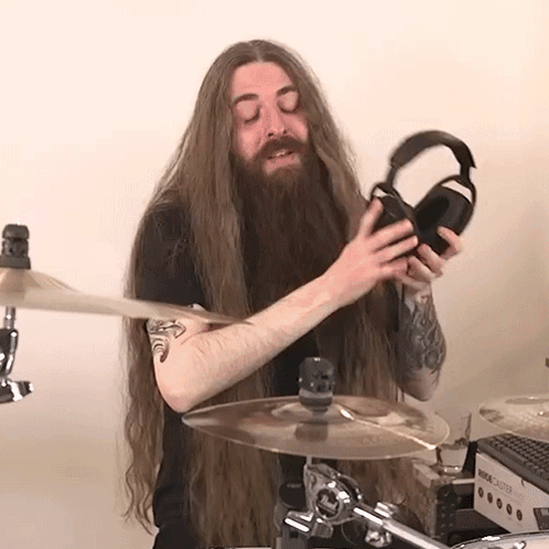 A Man With Long Hair And A Beard Is Holding A Pair Of Headphones While Playing Drums GIF