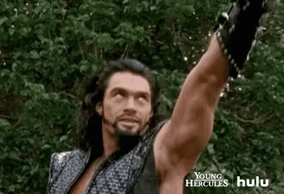 A Man With Long Hair And A Beard Is Holding A Sword In The Air . GIF