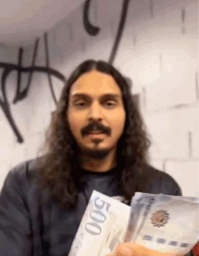A Man With Long Hair And A Beard Is Holding Up A 500 Bill GIF