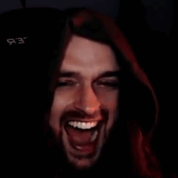 A Man With Long Hair And A Beard Is Laughing In A Dark Room With A Black Background GIF