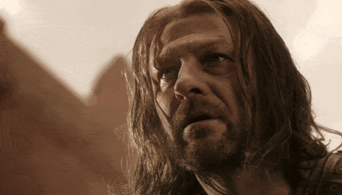 A Man With Long Hair And A Beard Is Looking At Something GIF