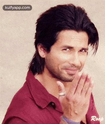 A Man With Long Hair And A Beard Is Making A Funny Face With His Hands Folded . GIF