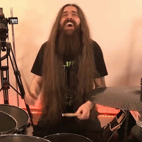 A Man With Long Hair And A Beard Is Playing A Drum Set GIF