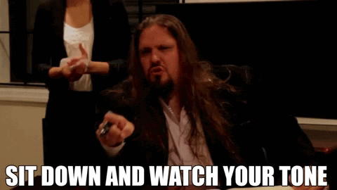 A Man With Long Hair And A Beard Is Sitting Down And Says Sit Down And Watch Your Tone GIF
