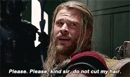 a man with long hair and a beard is sitting in a chair and talking to another man .