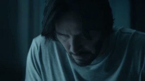 a man with long hair and a beard is sitting in a dark room .