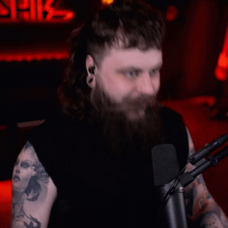 A Man With Long Hair And A Beard Is Sitting In Front Of A Microphone GIF