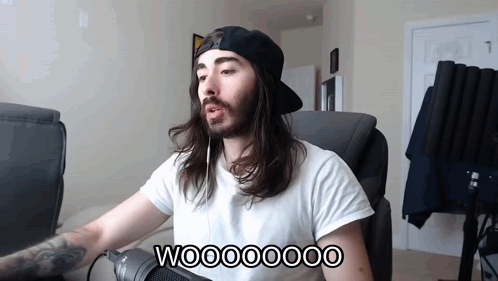 A Man With Long Hair And A Beard Is Sitting In Front Of A Microphone With The Words Wooooooo On The Bottom GIF