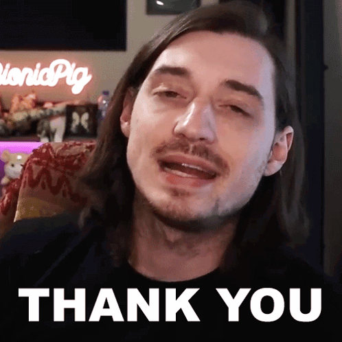 A Man With Long Hair And A Beard Is Sitting In Front Of A Thank You Sign GIF