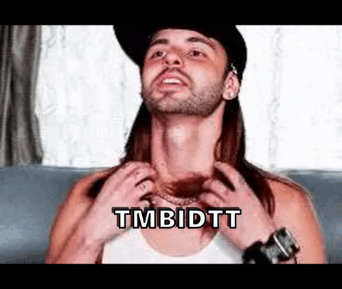 A Man With Long Hair And A Beard Is Sitting On A Couch Adjusting His Shirt . GIF