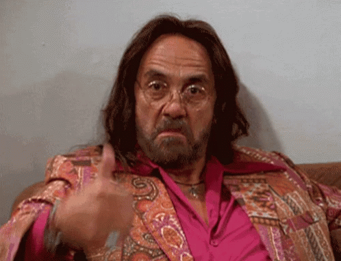 A Man With Long Hair And A Beard Is Sitting On A Couch And Giving A Thumbs Up GIF