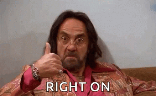 A Man With Long Hair And A Beard Is Sitting On A Couch And Giving A Thumbs Up . GIF