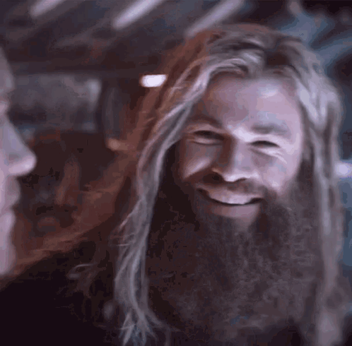 A Man With Long Hair And A Beard Is Smiling While Looking At Another Man . GIF