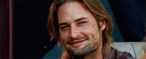 A Man With Long Hair And A Beard Is Smiling While Sitting On A Couch . GIF