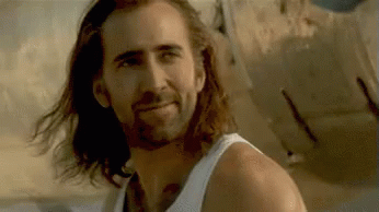 A Man With Long Hair And A Beard Is Smiling While Wearing A White Tank Top . GIF