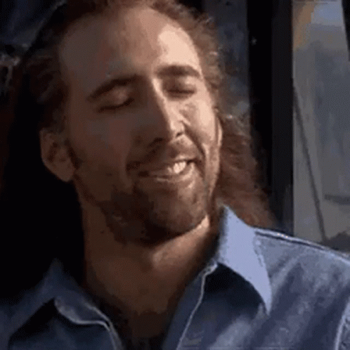 A Man With Long Hair And A Beard Is Smiling With His Eyes Closed In A Blue Shirt . GIF