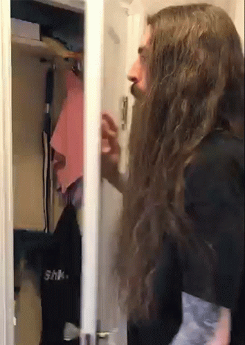 A Man With Long Hair And A Beard Is Standing In A Closet GIF