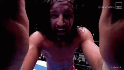 a man with long hair and a beard is standing in a ring with his arms in the air .