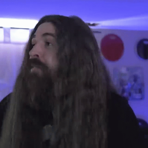 A Man With Long Hair And A Beard Is Standing In A Room GIF