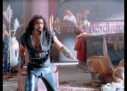A Man With Long Hair And A Beard Is Standing In A Room With Candles On A Table . GIF