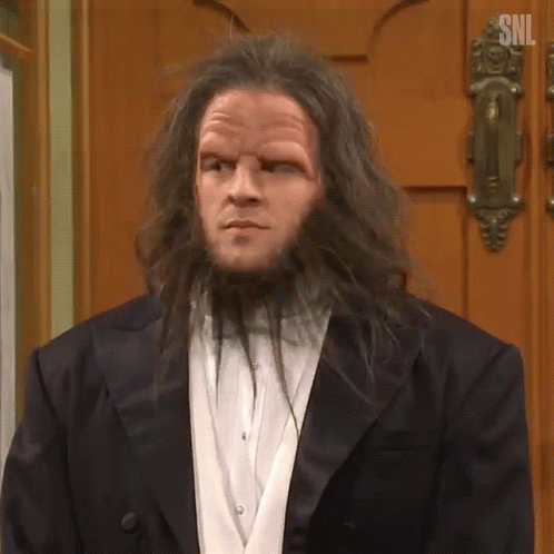A Man With Long Hair And A Beard Is Standing In Front Of A Door . GIF