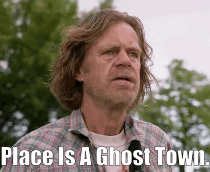 A Man With Long Hair And A Beard Is Standing In Front Of Trees And Says Place Is A Ghost Town . GIF