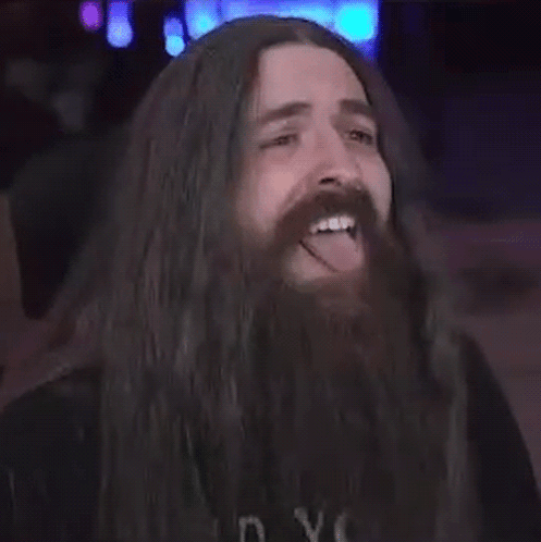A Man With Long Hair And A Beard Is Sticking Out His Tongue . GIF