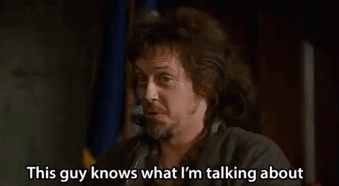 A Man With Long Hair And A Beard Is Talking On A Cell Phone While Holding A Gun . GIF