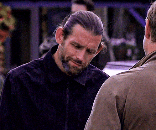 A Man With Long Hair And A Beard Is Talking To Another Man In A Brown Jacket GIF