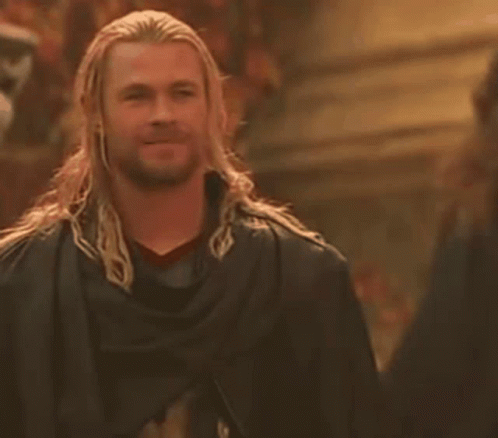 A Man With Long Hair And A Beard Is Wearing A Black Cape And Smiling . GIF
