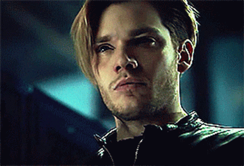 A Man With Long Hair And A Beard Is Wearing A Black Leather Jacket And Looking At The Camera . GIF