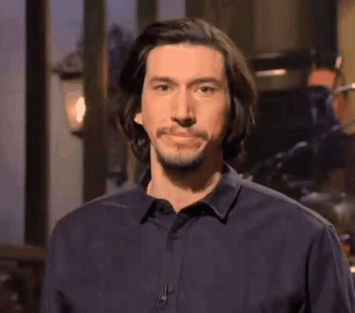 A Man With Long Hair And A Beard Is Wearing A Black Shirt And Looking At The Camera . GIF