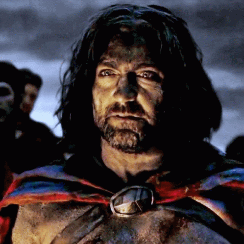 A Man With Long Hair And A Beard Is Wearing A Cape And A Medallion Around His Neck GIF