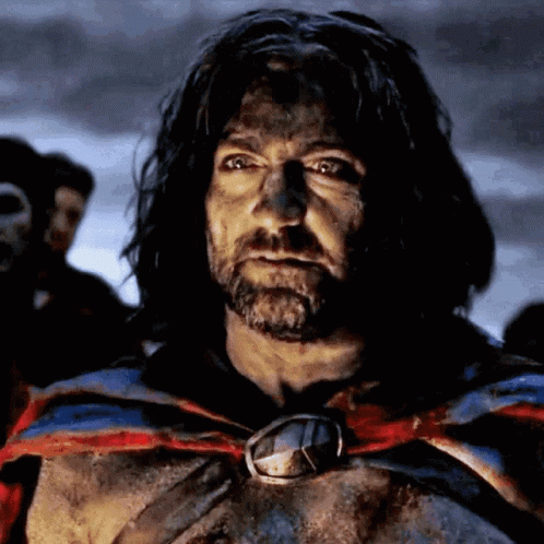 A Man With Long Hair And A Beard Is Wearing A Cape With A Medallion Around His Neck GIF