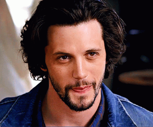 A Man With Long Hair And A Beard Is Wearing A Denim Jacket GIF