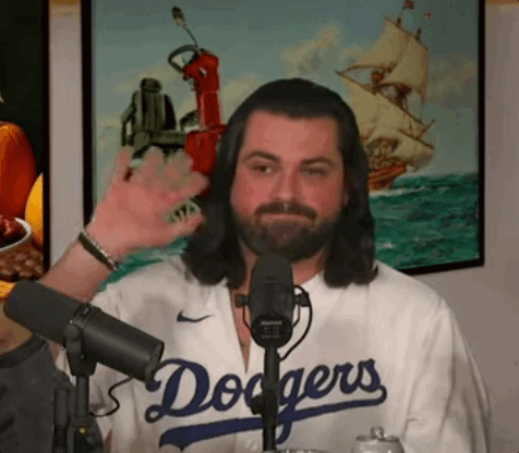 A Man With Long Hair And A Beard Is Wearing A Dodgers Jersey And Waving At The Camera . GIF